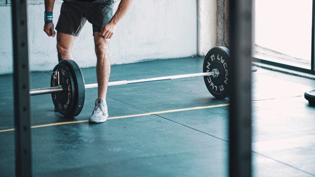man in black t-shirt and black shorts holding black barbell